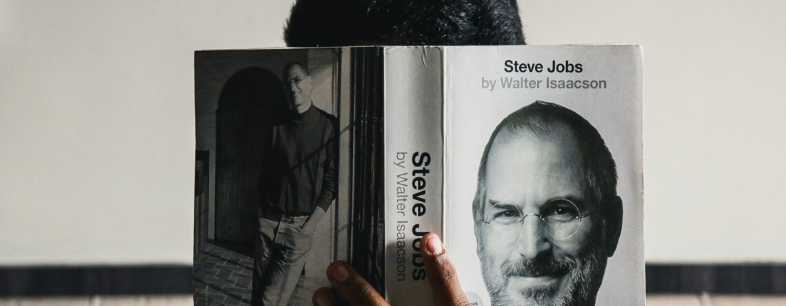 guy reading a book about steve jobs, there is a picture of him on the book cover