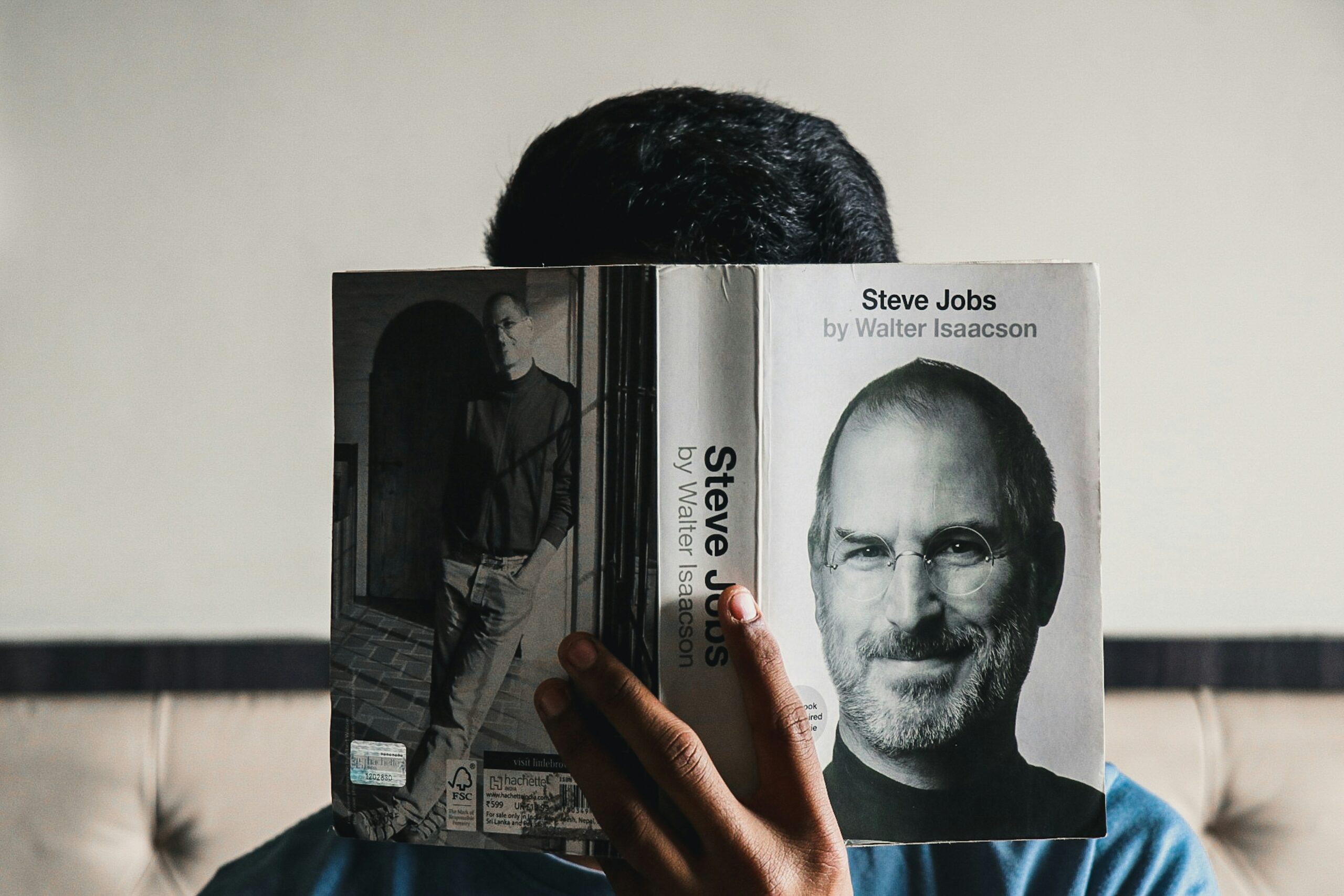 guy reading a book about steve jobs, there is a picture of him on the book cover